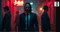 A man in a suit stands in a dimly lit alleyway, surrounded by other people in suits, with a red neon sign in the background.