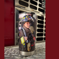 A firefighter in full gear is smiling and holding a fire hose, with a fire truck visible in the background.