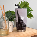 a tall, black and white Eiffel Tower printed on a stainless steel tumbler with a black handle, placed on a wooden surface.
