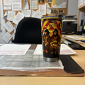 A firefighting-themed tumbler cup sits on a cluttered desk, surrounded by various papers and office supplies.